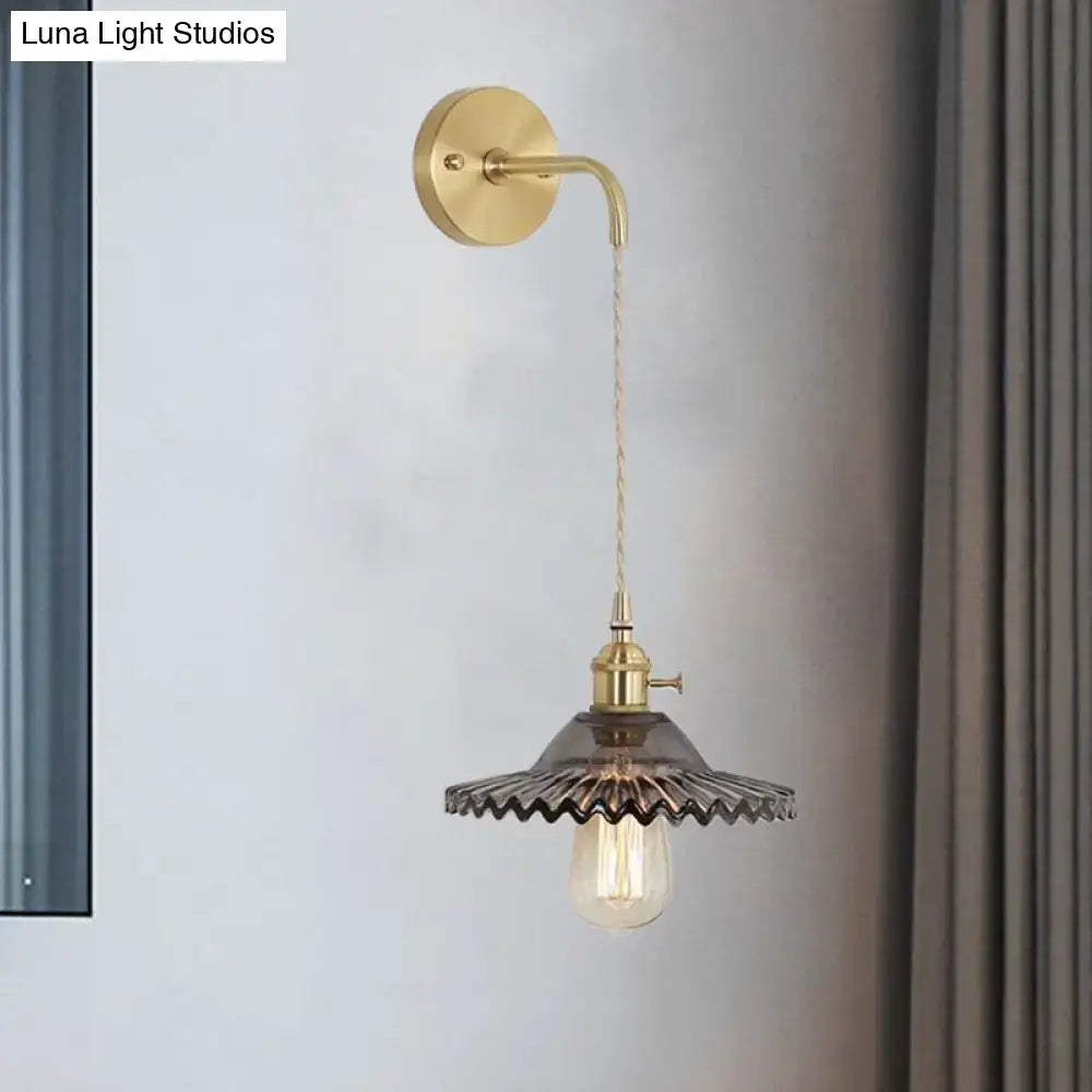 Industrial smoked glass brass sconce light featuring a gold-toned brass sconce light with dark scalloped glass shade