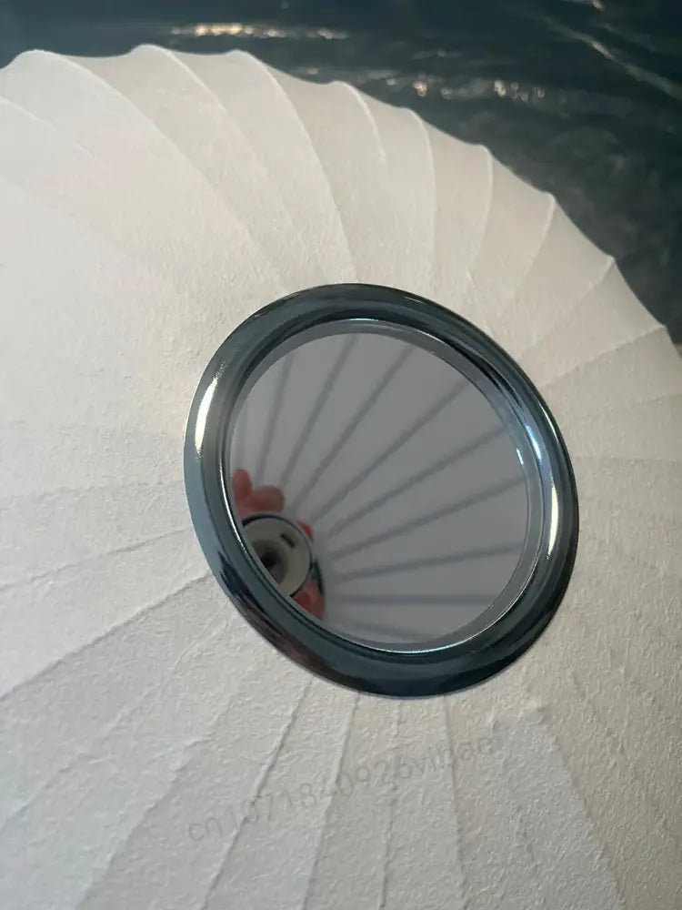 A sleek chrome circular decorbites™ silk led pendant lamp resting on white pleated fabric with modern design