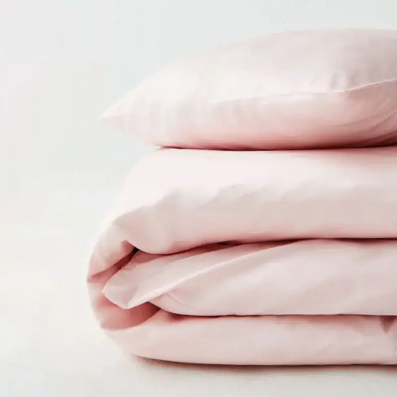 A soft blush pink satin pillowcase resting on a matching silky cooling duvet cover set by decorbites