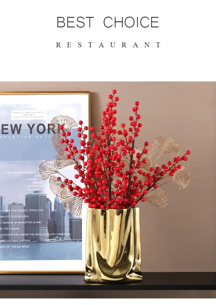 Gold metallic vase with sculpted wavy sides holding red berries and gold leafed branches in a silver ruffled flower vase