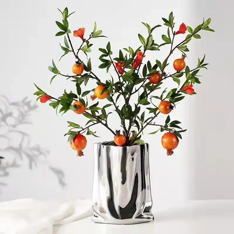 Decorbites™ silver ruffled ceramic flower vase with a sleek metallic finish holding pomegranate branches with orange fruits