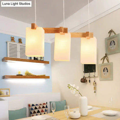 Modern wooden pendant light with three warm-toned opaline glass shades and adjustable chain cord length for island use