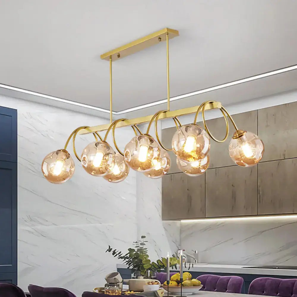 Gold-toned DecorBites™ sleek gold spiral island light with spherical amber glass globes and curved metal arms