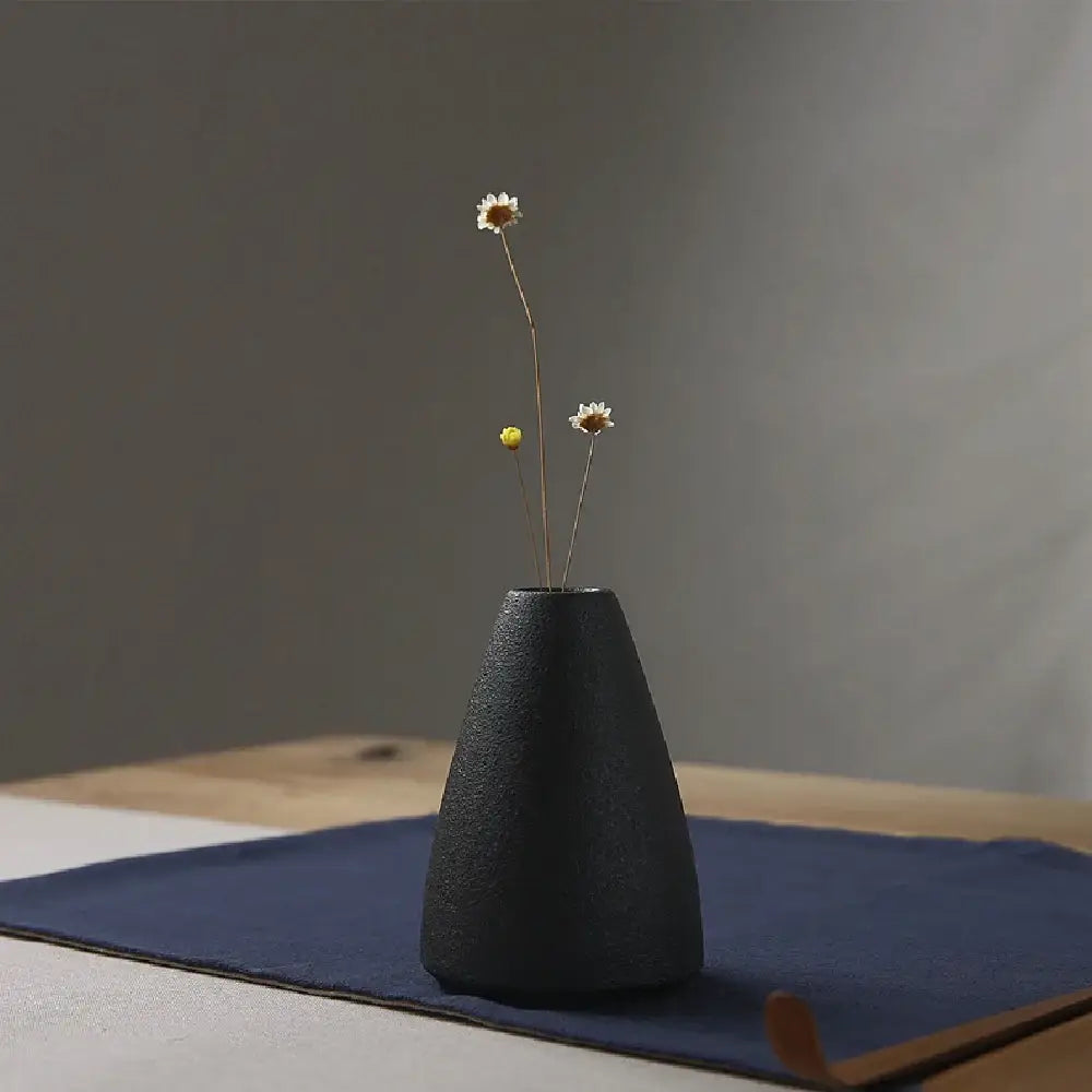 Black textured ceramic small vase holding dried white and yellow flowers for elegant japanese home decor