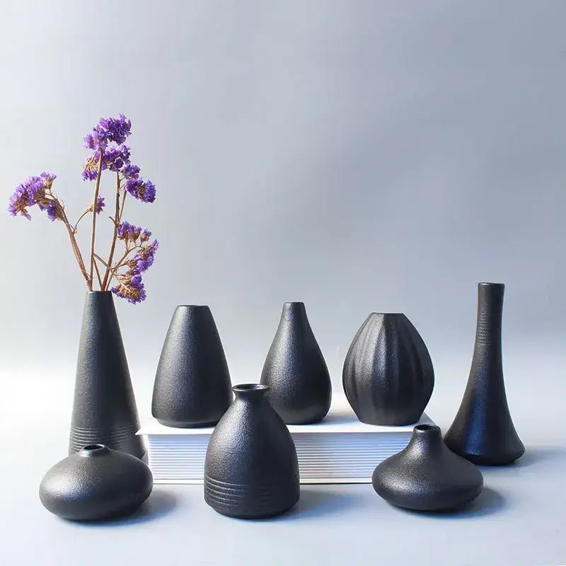 A collection of matte black ceramic small vases in organic shapes for elegant japanese home decor with dried purple flowers