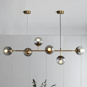 Modern brass finish pendant light with smoke grey glass and six spherical bulbs ideal for restaurants