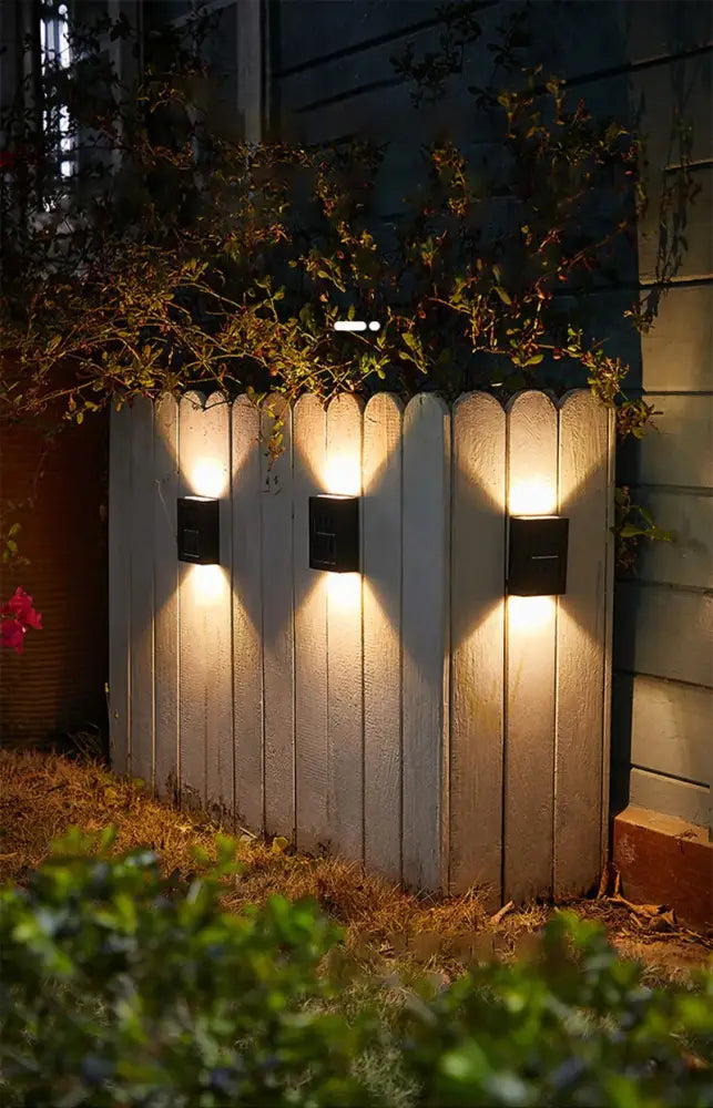 Decorbites solar led outdoor wall light with black lamp beads illuminating a weathered white wooden fence
