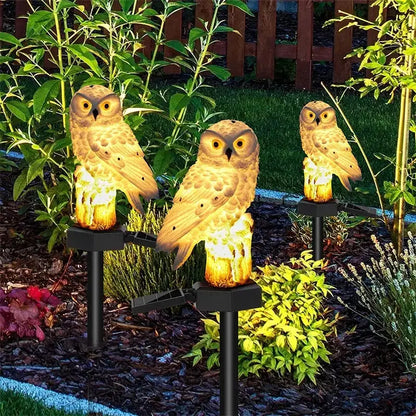 Three illuminated tan owl garden lights with solar panels and black stakes from decorbites solar owl garden light