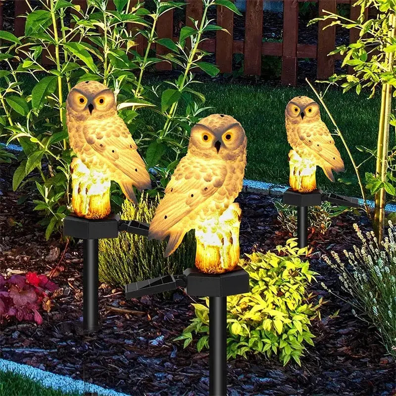 Three illuminated tan owl garden lights with solar panels and black stakes from decorbites solar owl garden light
