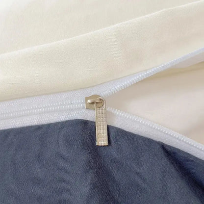 A metallic zipper pull with a textured grid pattern on the seam of a cream and navy blue decorbites™ solid color brush fabric duvet cover