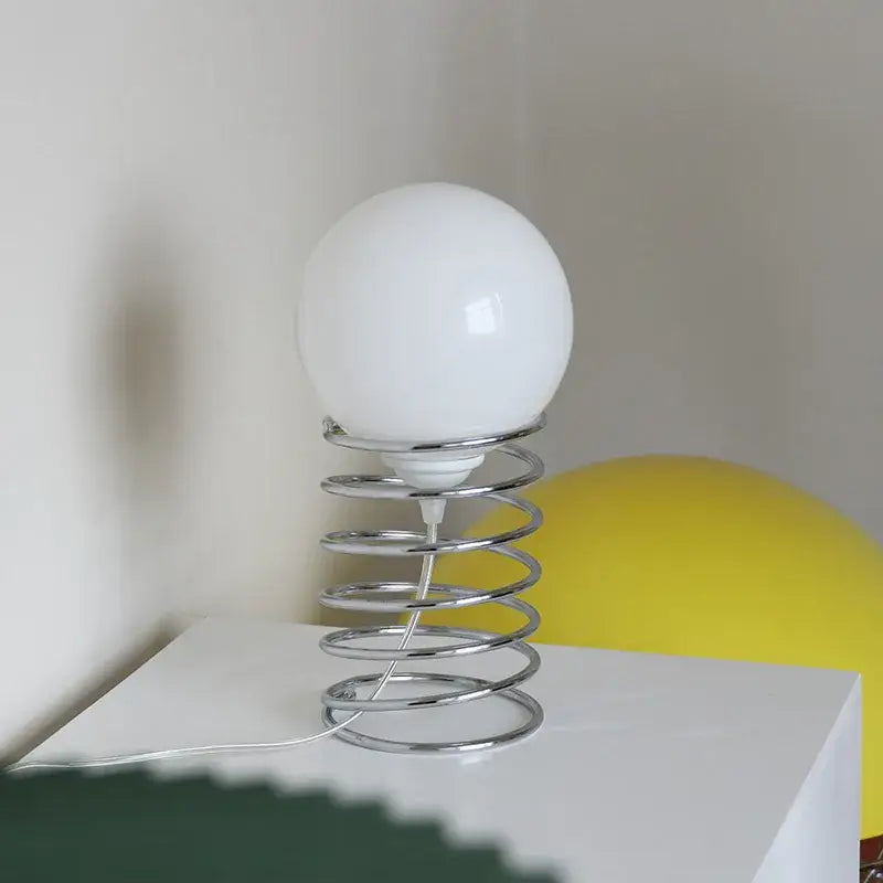 DecorBites™ spring glass table lamp with a sleek chrome spring base and smooth opaque white glass lampshade