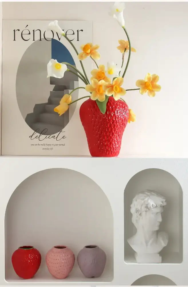 A vibrant red ceramic strawberry cartoon flower vase holding yellow and white calla lilies by DecorBites