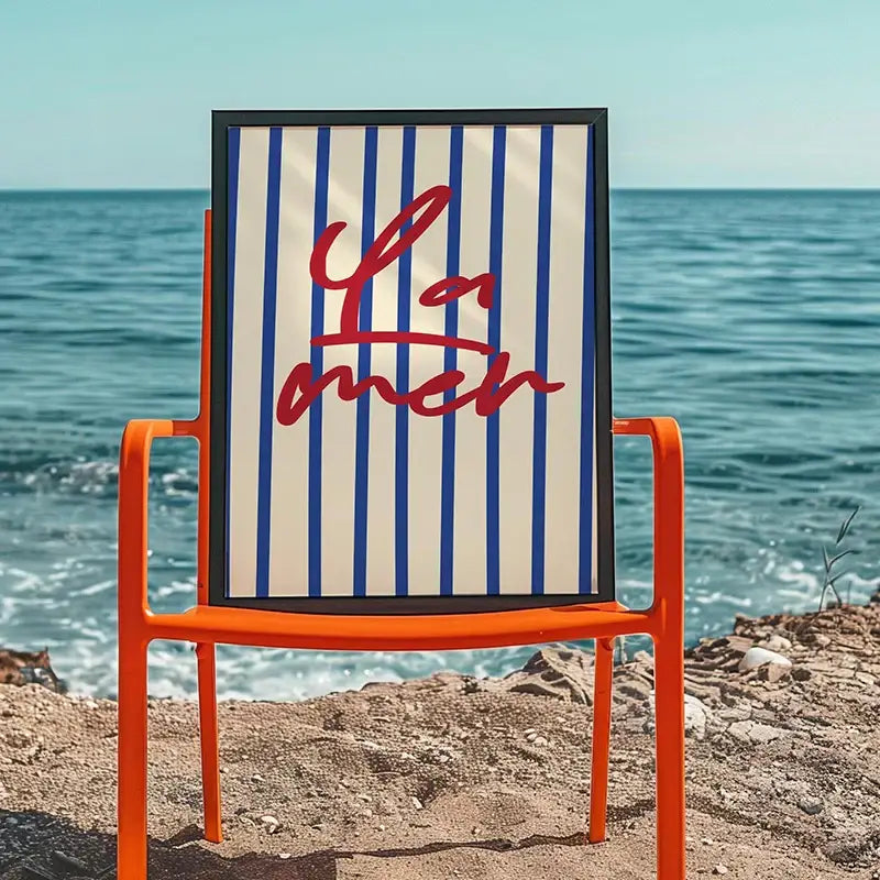 Orange metal chair with framed beach canvas artwork featuring blue white stripes and red script from DecorBites summer vibe posters