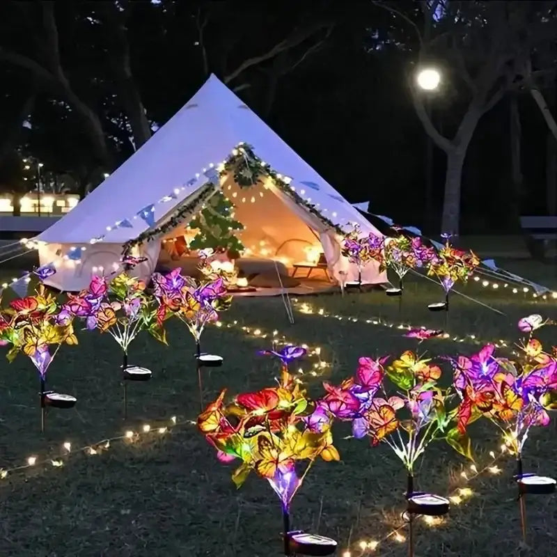 A white bell tent lit from within with decorbites™ sunflower solar garden lights shaped like colorful butterflies around it