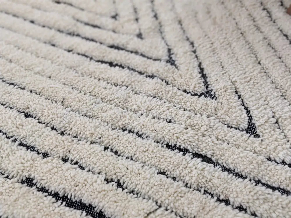 Cream-colored tapis beni ouarain with plush textured surface and bold black geometric diagonal stripes by DecorBites