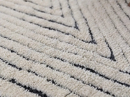 Cream-colored tapis beni ouarain with plush textured surface and bold black geometric diagonal stripes by DecorBites