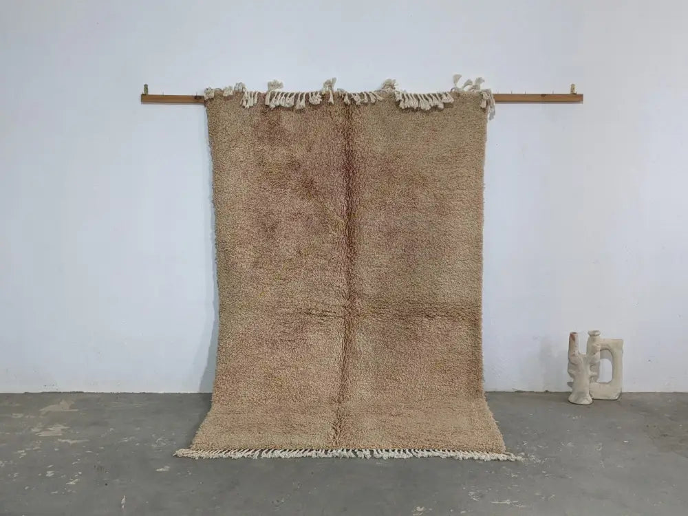 Beige plush wool tapis beni ouarain with fringed edges hanging on wooden rod from decorbites collection