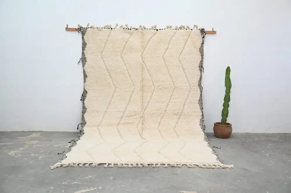 Cream-colored beni ouarain traditional tapis beni with textured handwoven surface and bold black zigzag fringed edges