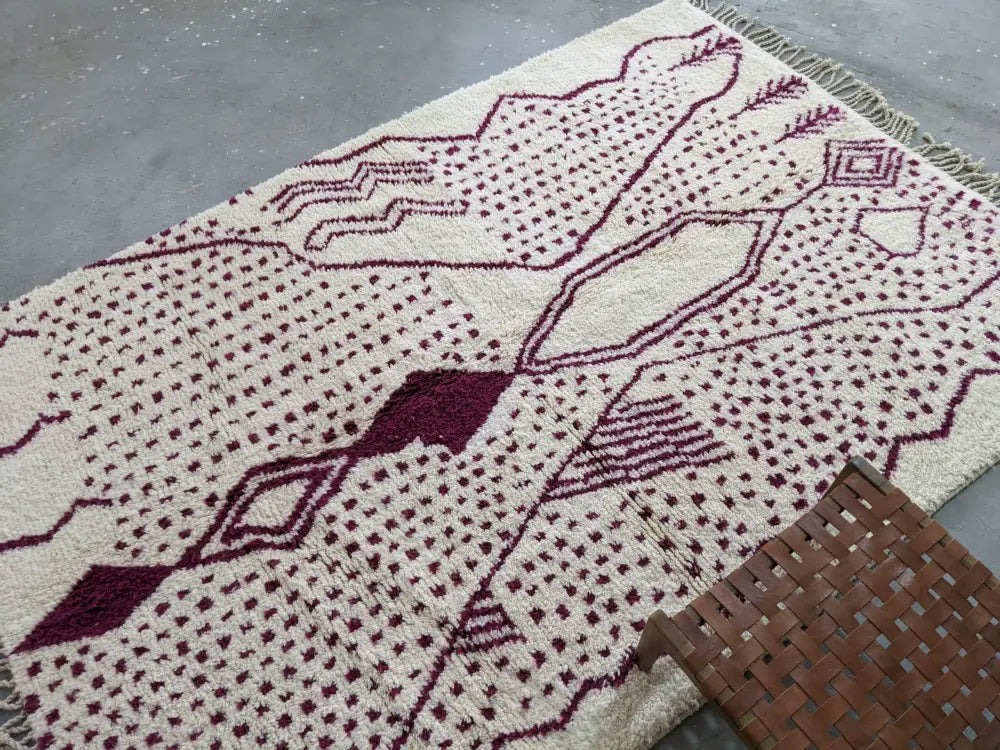 Cream-colored tapis beni ouarain rug with deep burgundy geometric patterns and fringed edges by DecorBites™