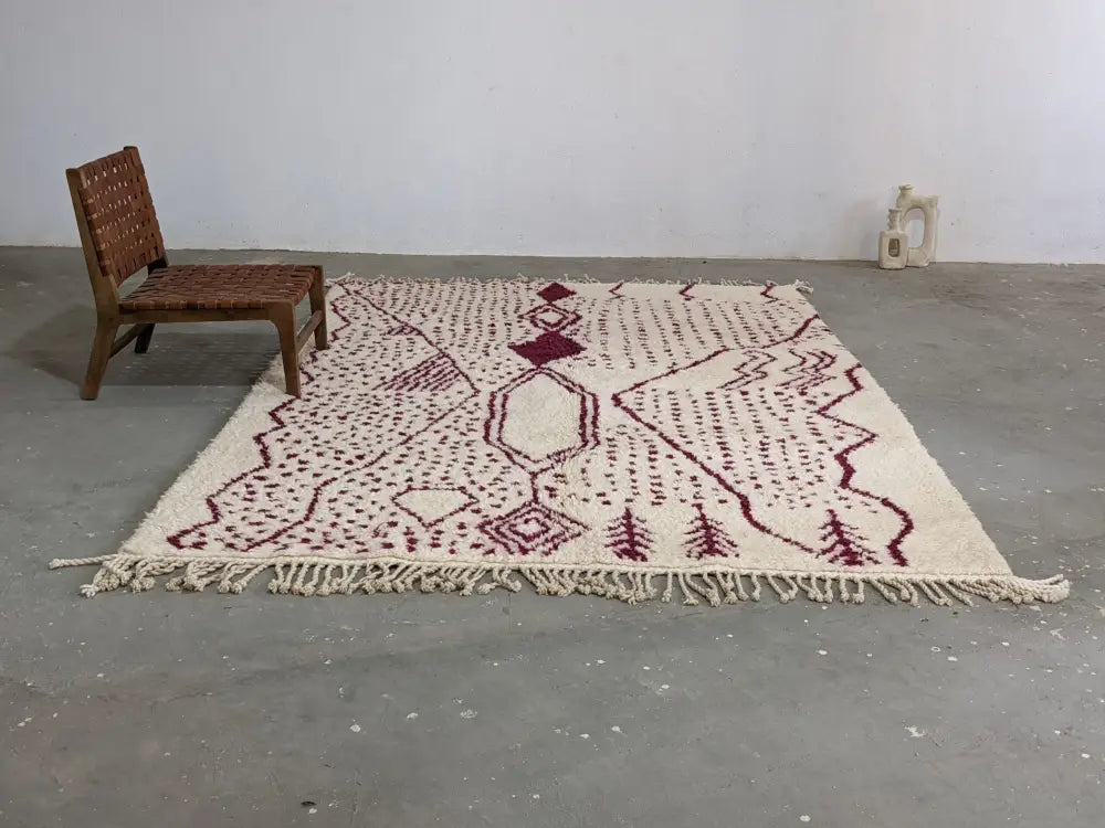 Cream-colored beni ouarain tapis featuring intricate maroon geometric and tree motifs with fringed edges by DecorBites