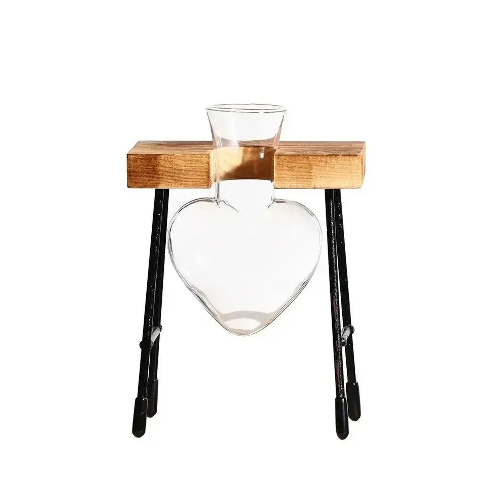 Clear glass heart-shaped vase with narrow neck on wooden platform with metal legs for avocado seed starter use
