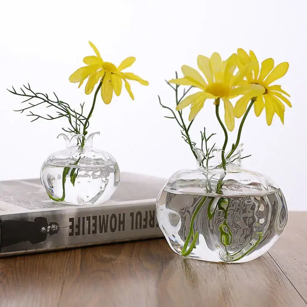 Clear glass DecorBites™ avocado seed starter vase with faceted rounded shape holding vibrant yellow daisies