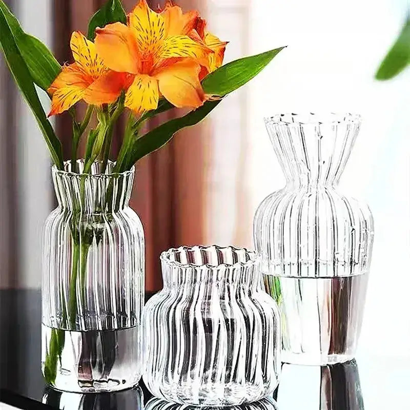 Clear glass transparent nordic vase with vertical ribbed pattern in varying heights holding orange alstroemeria flowers