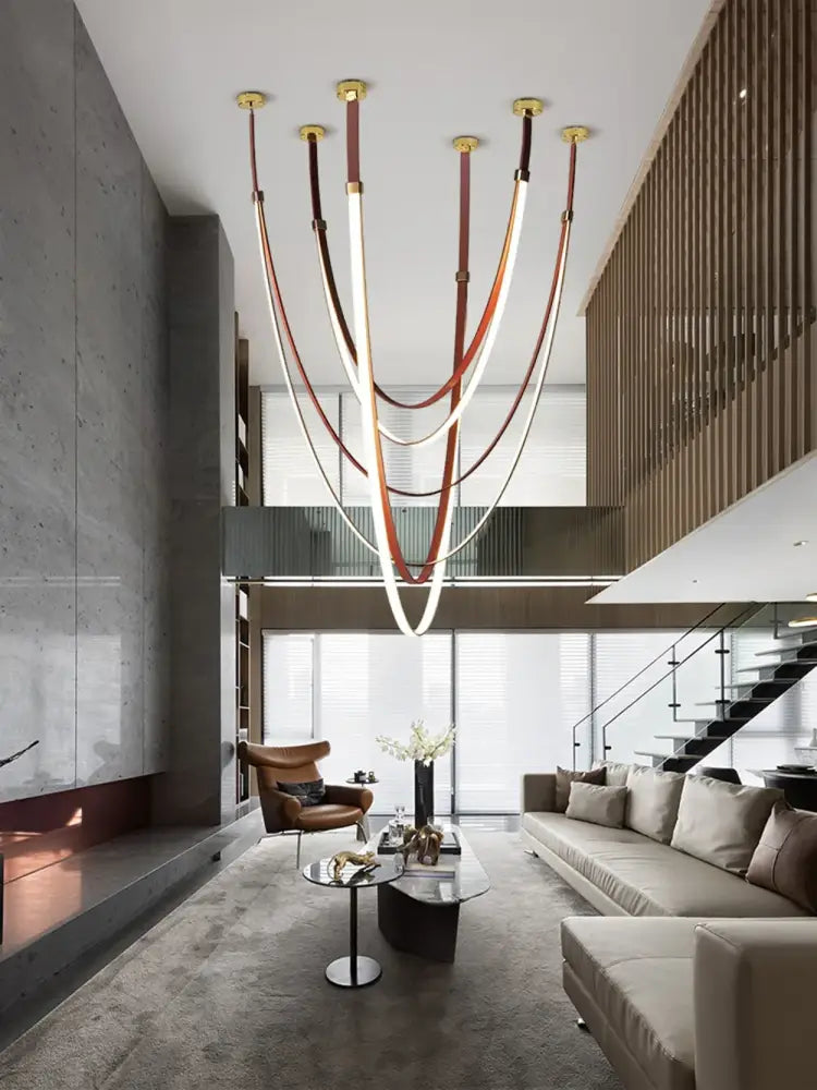 A modern decorbites™ led chandelier with multiple curved light tubes suspended by flexible leather belt straps and gold fixtures