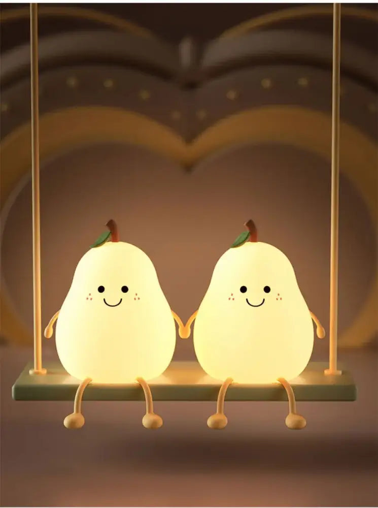 Two glowing pear-shaped silicone decorbites™ rechargeable night lights with smiling faces sitting on a swing