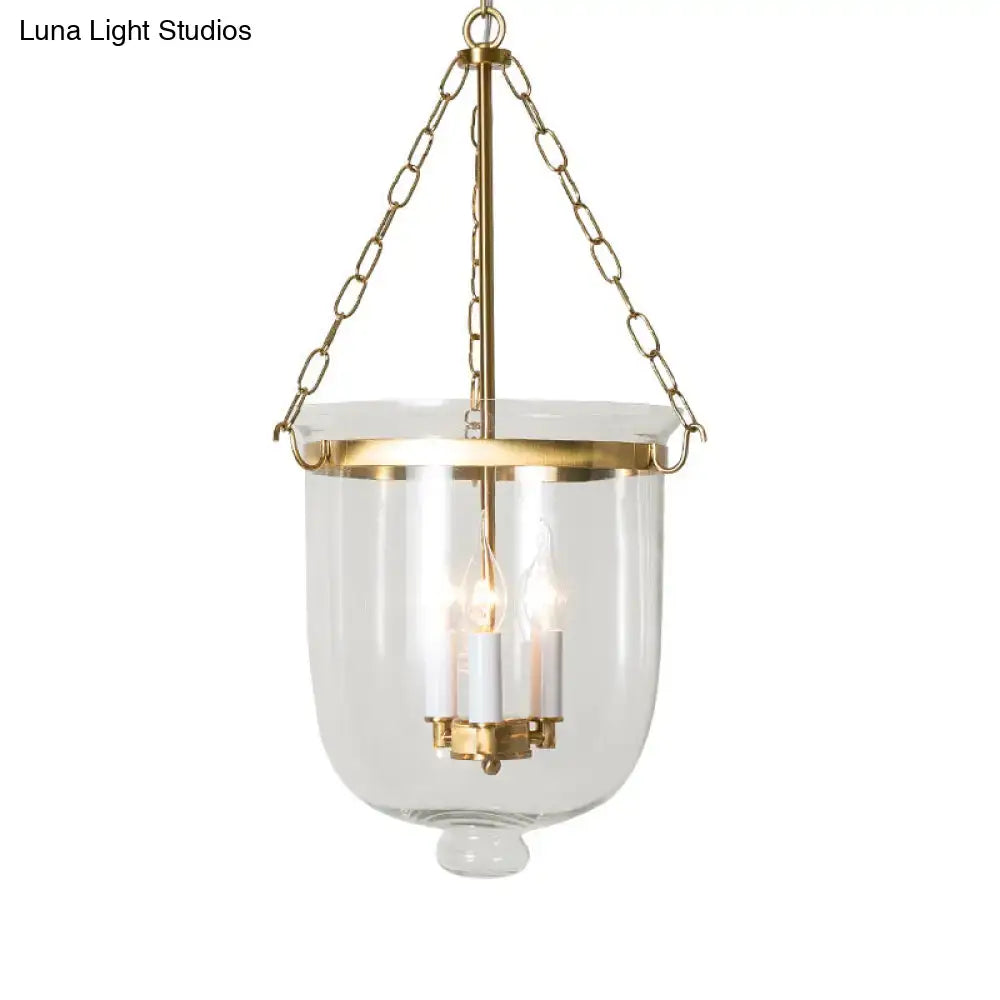 Gold-toned brass pendant lantern with clear glass body and inverted cloche design featuring chain cord length