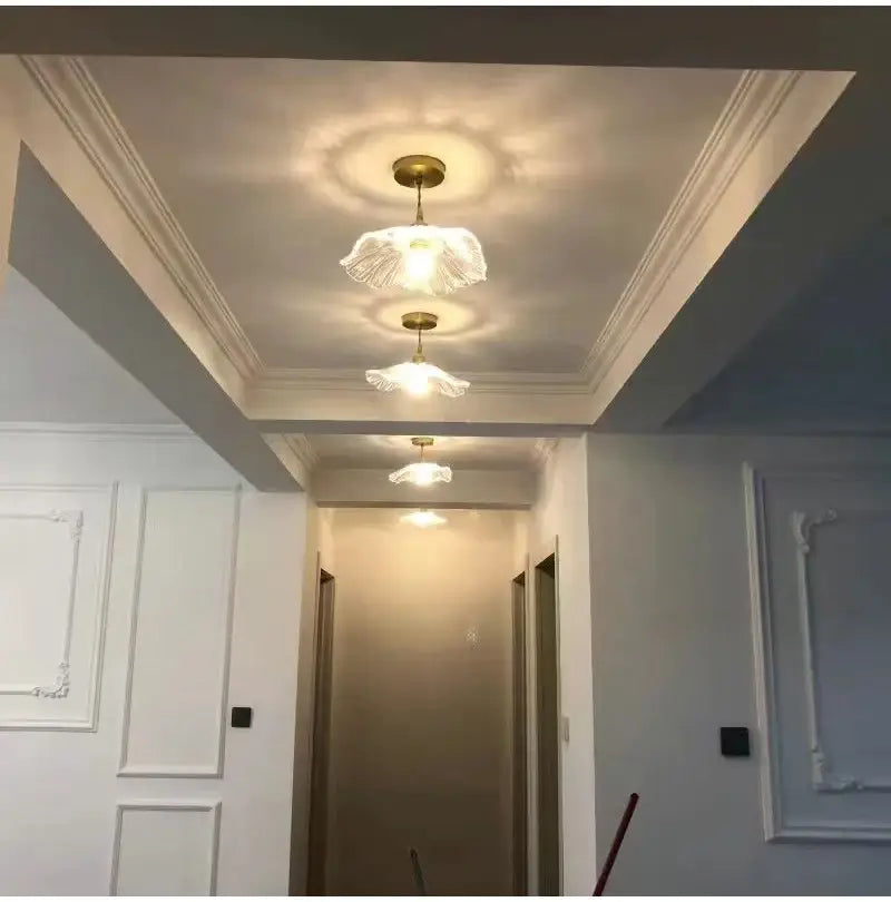 Three elegant translucent vintage flower glass pendant lights with gold fixtures hang in a hallway for home decor