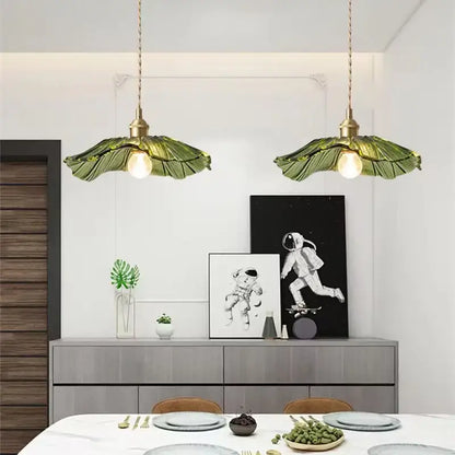 Two green leaf-shaped DecorBites™ pendant lights with brass fixtures hang above a dining table for home decor