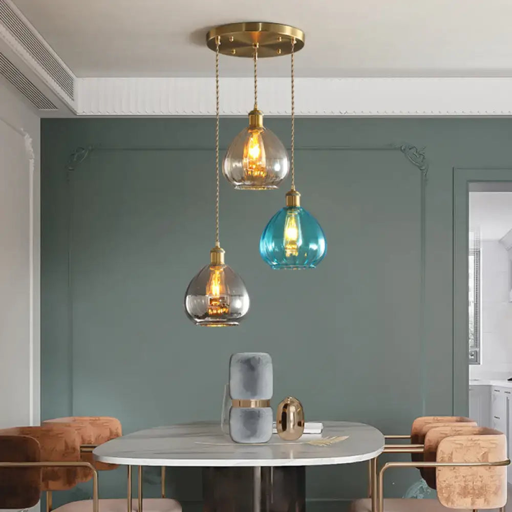 Three pendant lights with brass fixtures and glass onion multi teardrop shades in tan, blue, and grey hang from a ceiling mount