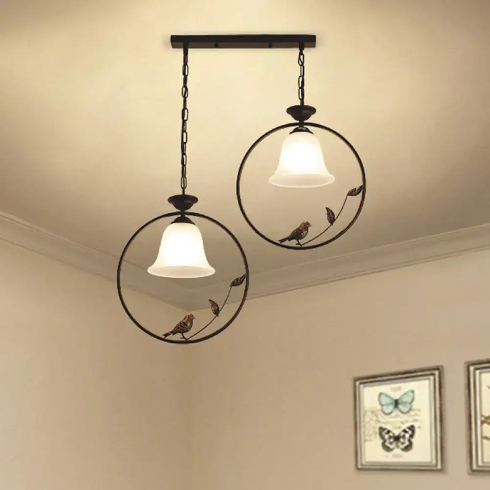 Two black wrought iron pendant lights with decorative bird accents and handblown glass flared shades for kitchen island lighting