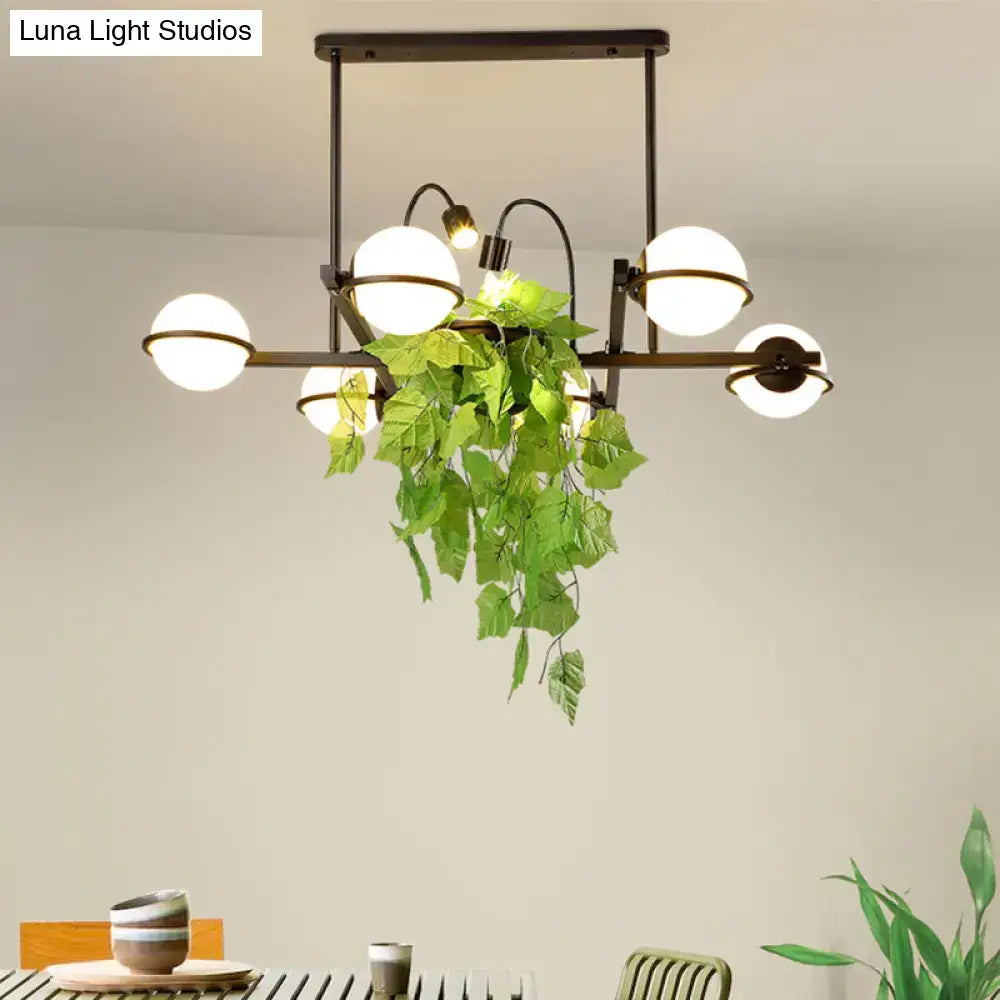 Modern black metal DecorBites island lighting fixture with white glass shades and hanging green artificial foliage for kitchen