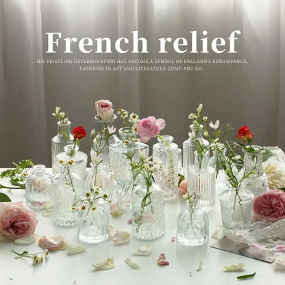 A collection of clear glass decorbites™ vintage relief vases with intricate patterns holding pink and white flowers