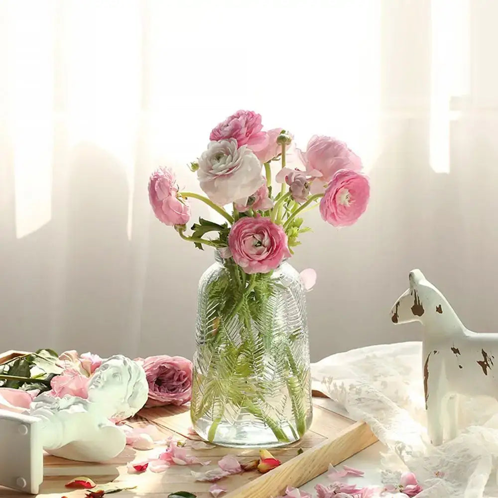 A clear glass vintage relief vase with textured leaf design holds pink and white ranunculus for hydroponic plants