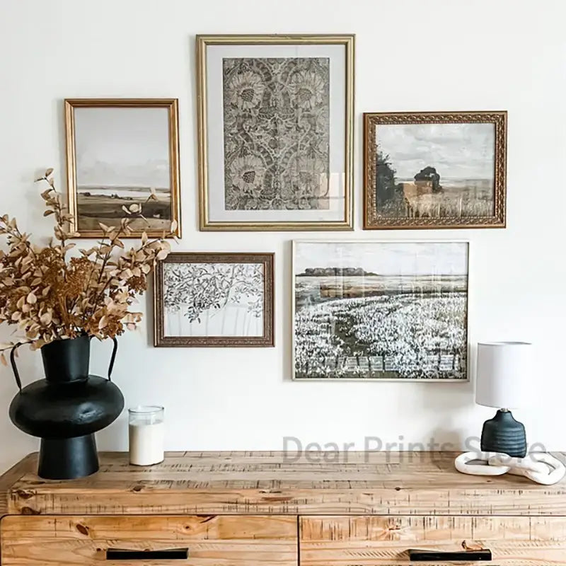 Set of five framed black and white summer landscape oil painting prints with ornate gold frames on a gallery wall above console table