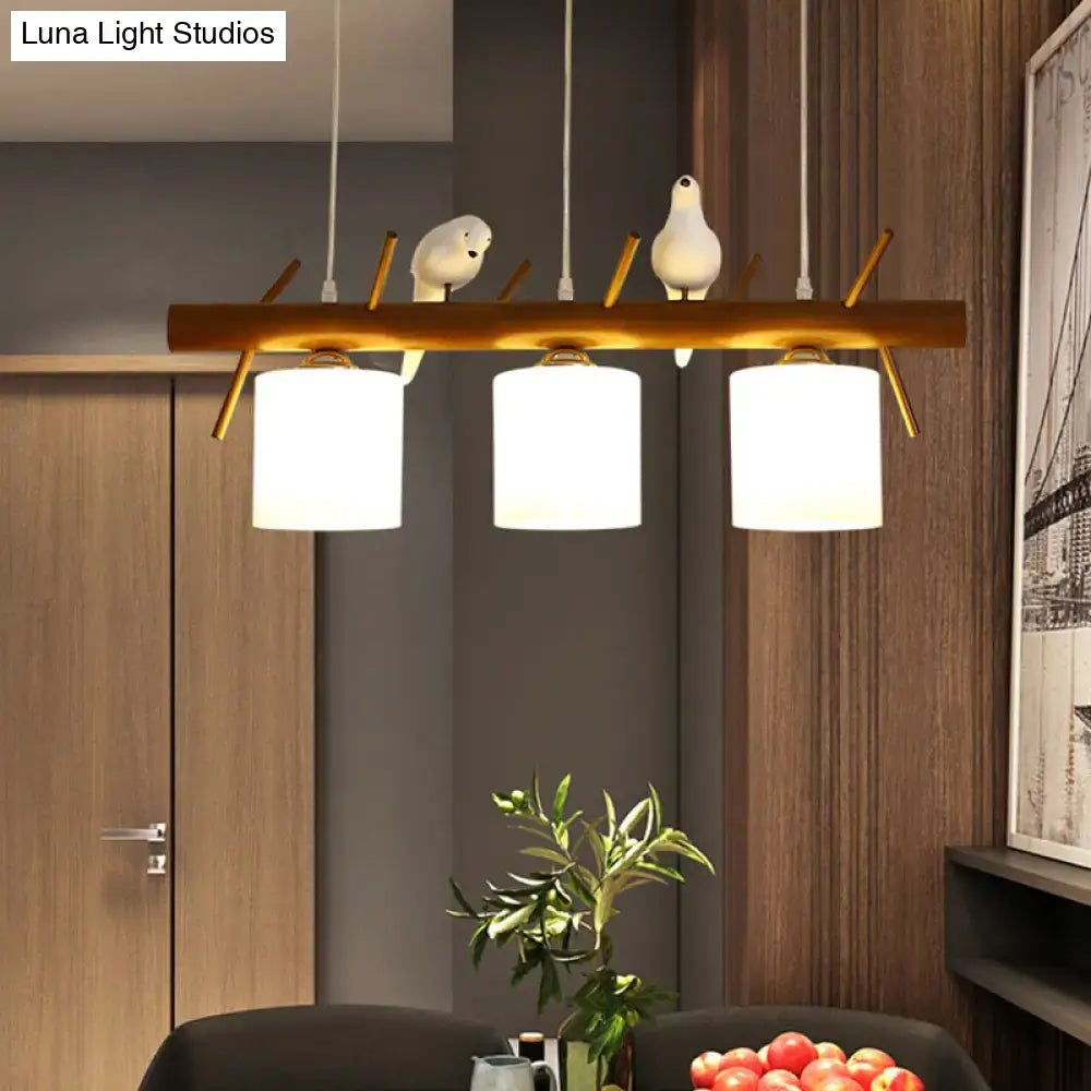 Modern wooden led pendant light with three white cylindrical shades and resin bird figurines on golden branches for cylinder restaurant use