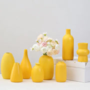 A collection of matte yellow porcelain flower vases for home decor with one holding white and pink flowers