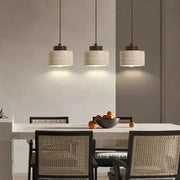 Three decorbites™ yellow stone led pendant chandeliers with off-white textured shades and dark metal fixtures above table