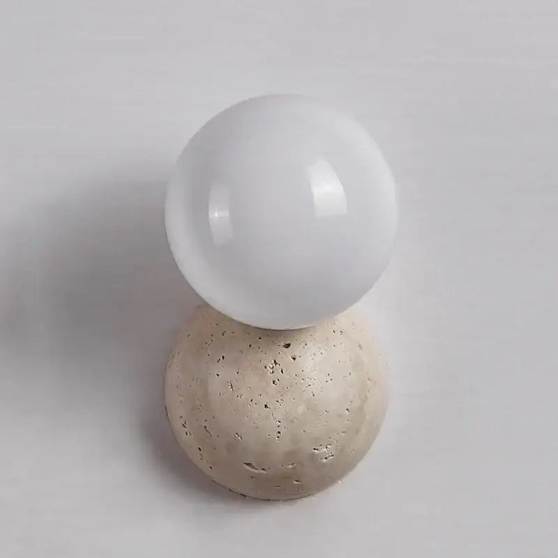 A sleek white glass sphere rests on a textured yellow travertine wall sconce base for modern bedroom decorbites lighting