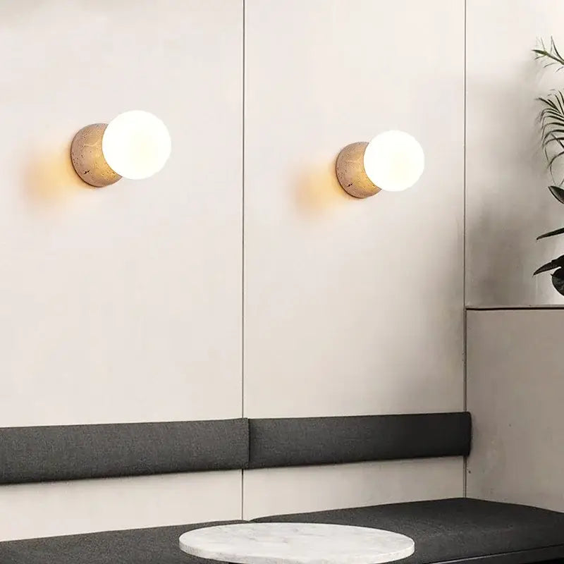 Two minimalist wall sconces with matte gold bases and glowing glass shades for modern yellow travertine bedroom decorbites wall sconce
