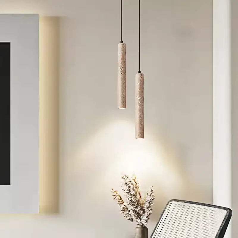 Two slender yellow travertine stone pendant lights with textured beige surface hang from black cords for kitchen island