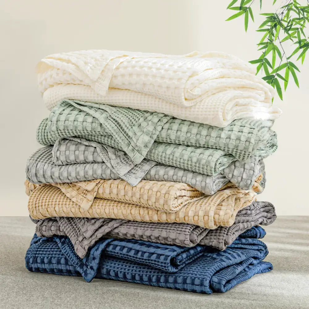 Stack of neatly folded bamboo cotton waffle bath towels in cream sage beige gray and navy blue for decorbites bamboo cotton blanket