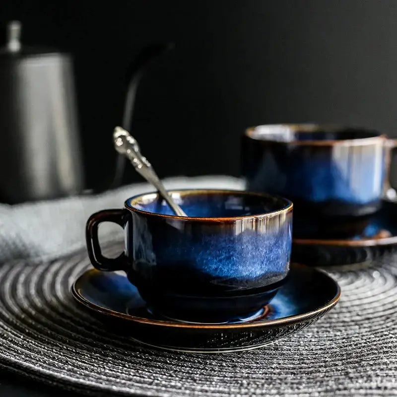 Deep blue glossy ceramic espresso coffee cup with brown rim resting on matching coffee cup saucer in dining room