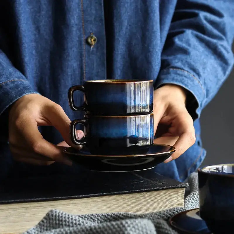 A pair of stacked deep blue glossy ceramic espresso coffee cups with subtle striations on matching cup saucer sets
