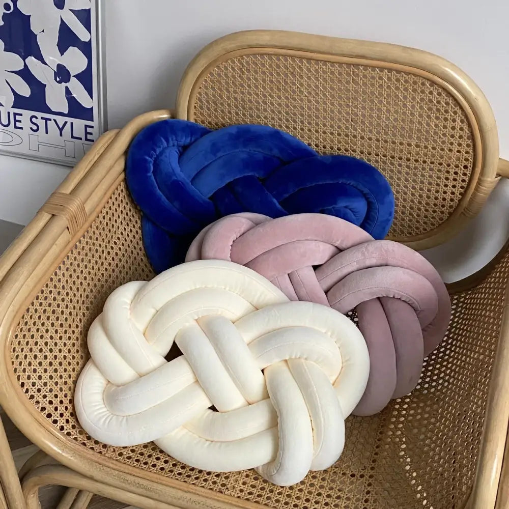 Three plush throw pillows in deep blue velvet, soft pink, and creamy white on a woven rattan chair decorbites blue handmade