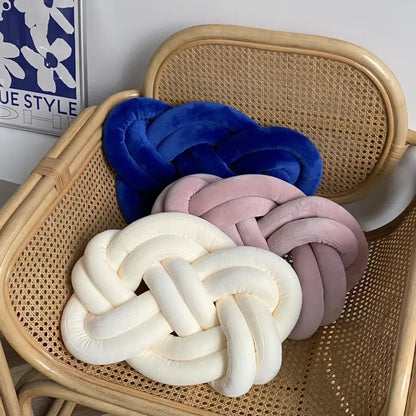 Three plush throw pillows in deep blue velvet, soft pink, and creamy white on a woven rattan chair decorbites blue handmade