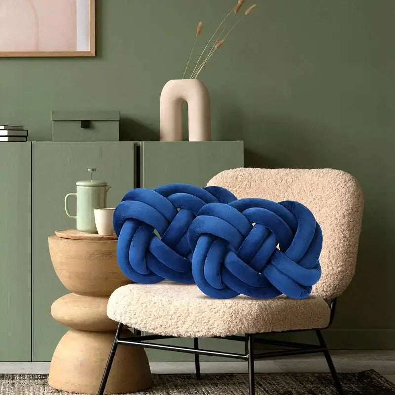 Vibrant blue handmade knot throw pillow in velvet resting on textured cream chair for living room decorbites decor
